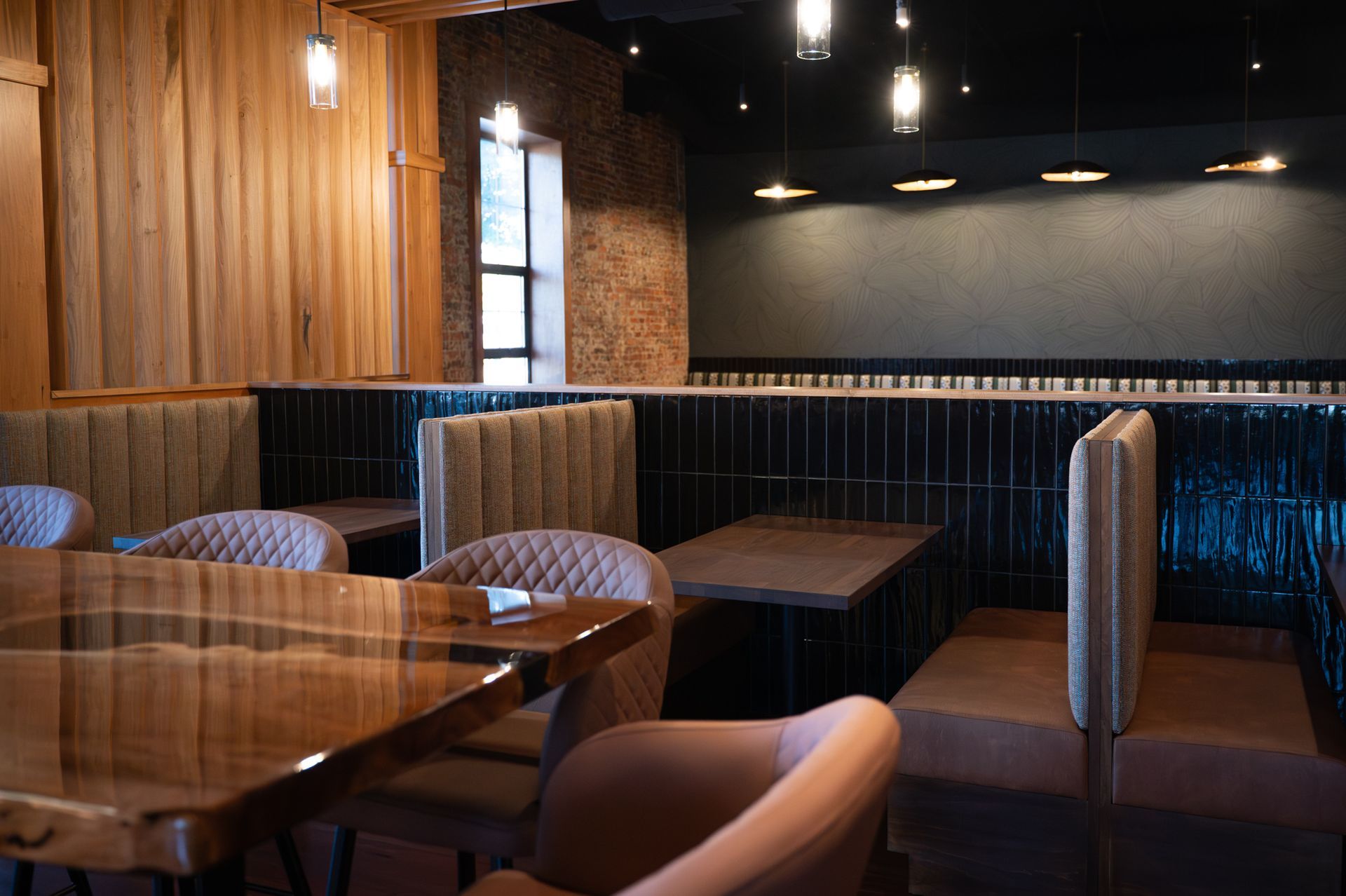 Empty modern restaurant booth with wooden walls, pendant lights, and blue-upholstered seating