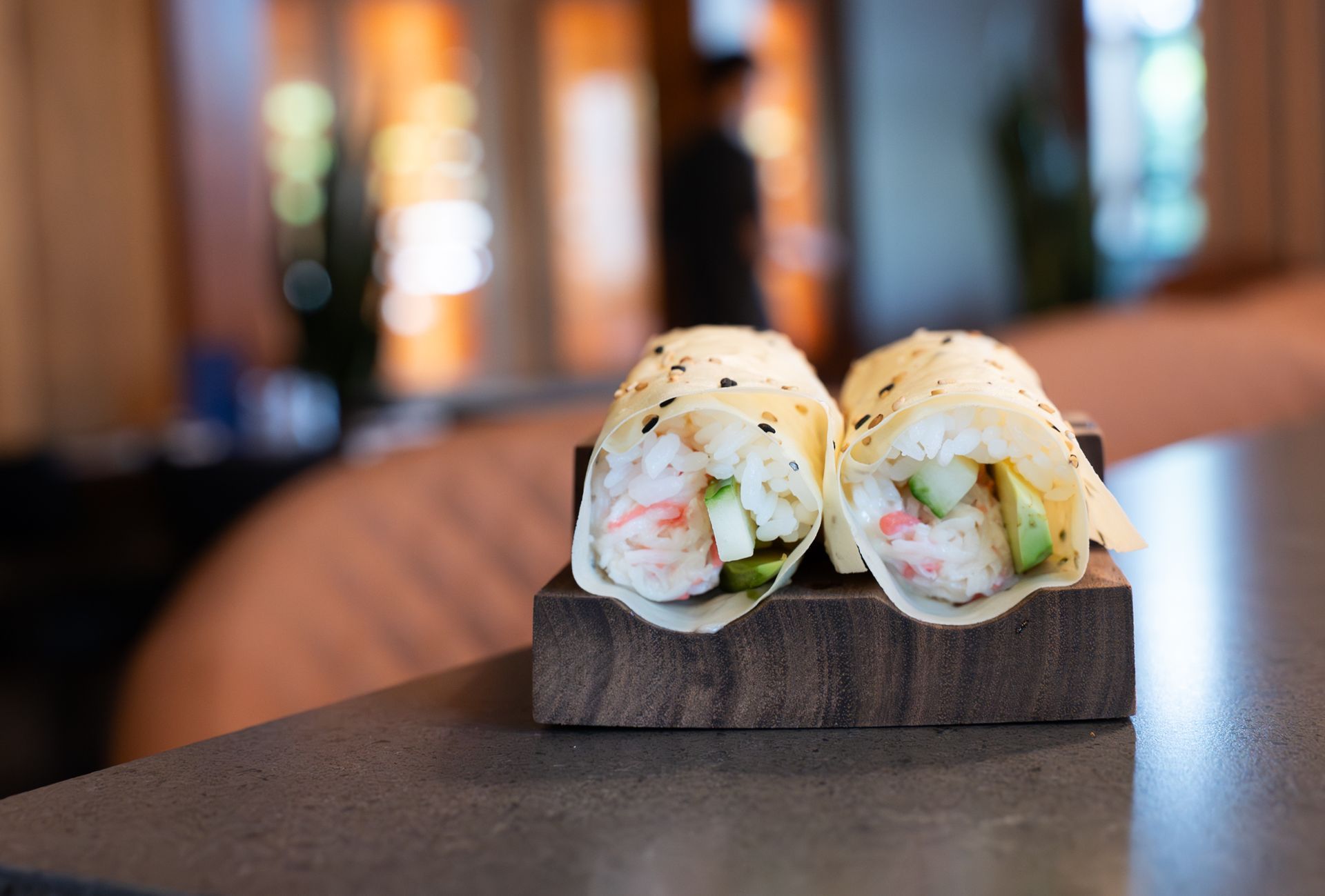 Two sushi rolls on a wooden stand with a blurred restaurant background