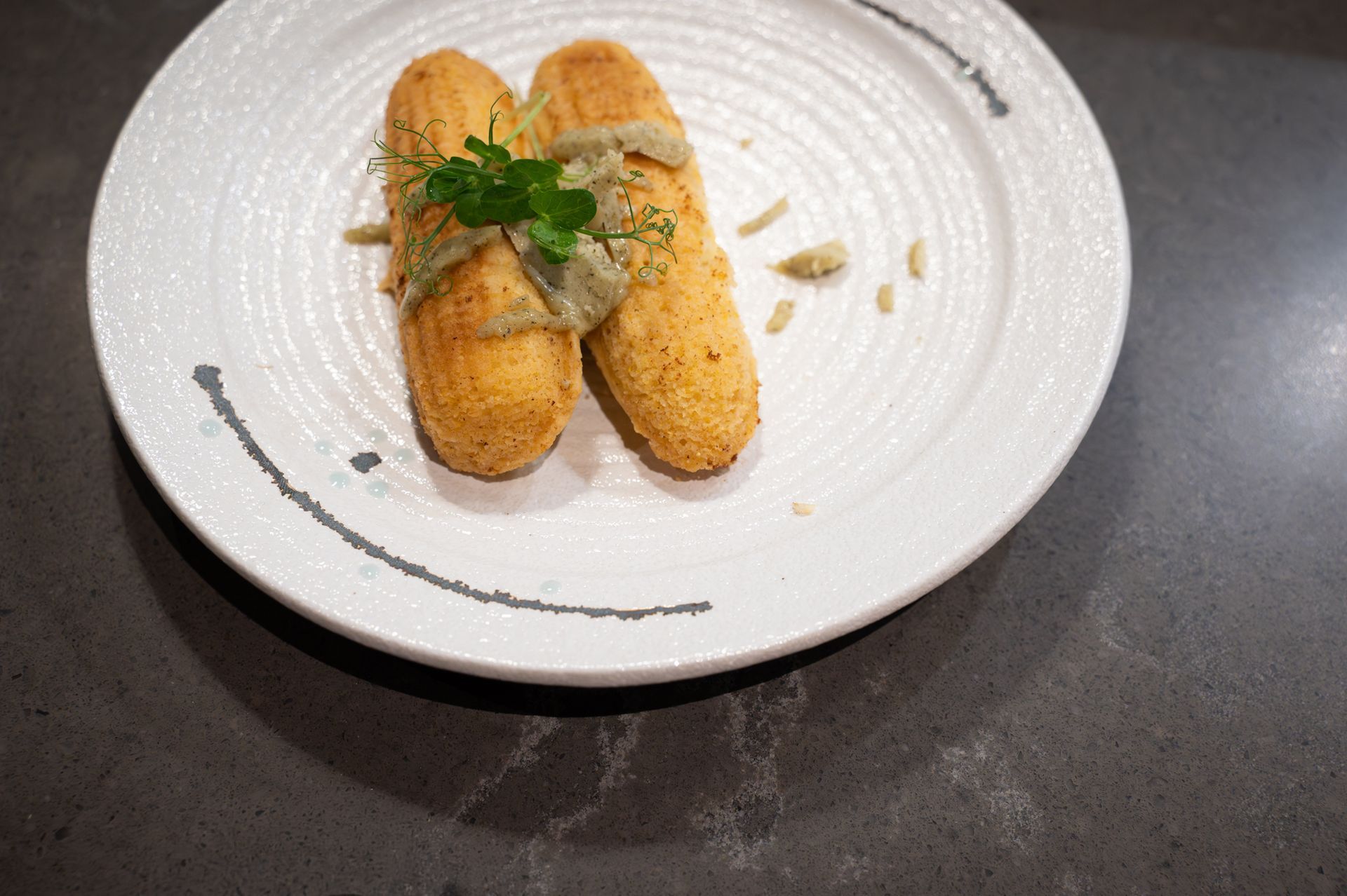 Two fried croquettes topped with parsley on a white plate with sauce drizzle