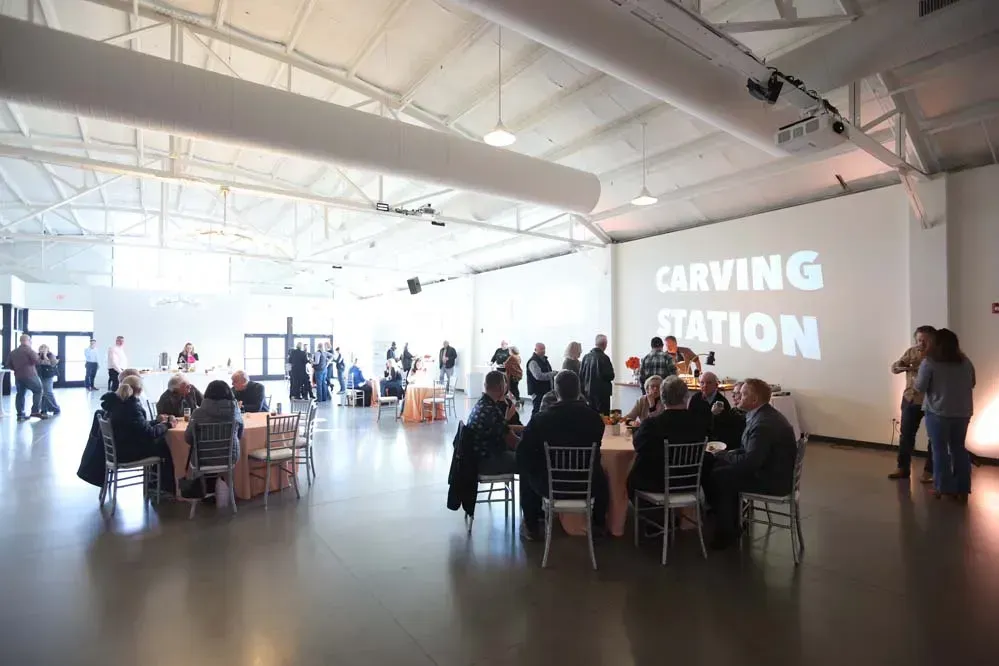 Large event space with tables, guests, and "CARVING STATION" projected on a wall.