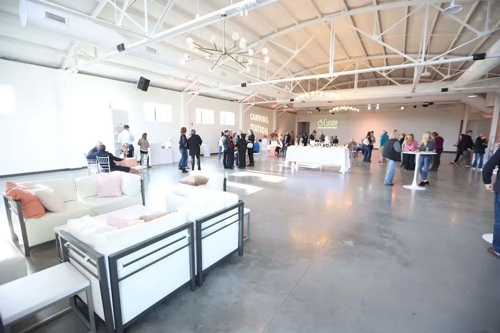 Large event space with white walls, concrete floor, and people mingling.