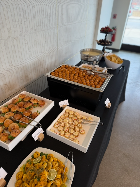 Buffet table with various appetizers: sliders, meatballs, shrimp, chips, and a cheese dip.