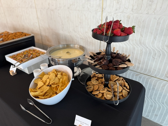 Buffet table with snacks: chips, soup, layered tray of strawberries, chocolate-covered pretzels, and cookies.
