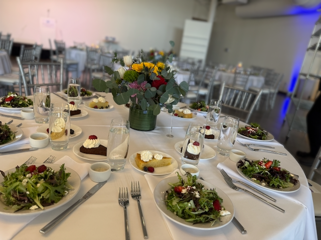 Elegant banquet table set with salads, desserts, and flowers in a bright room.