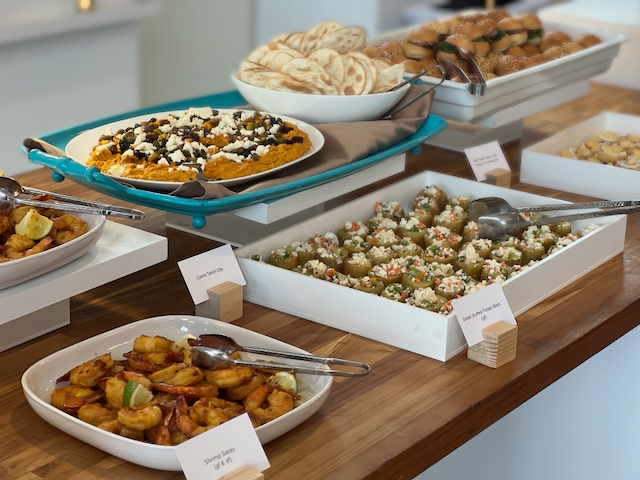Buffet table with various dishes: hummus, shrimp, olives, and pita bread.