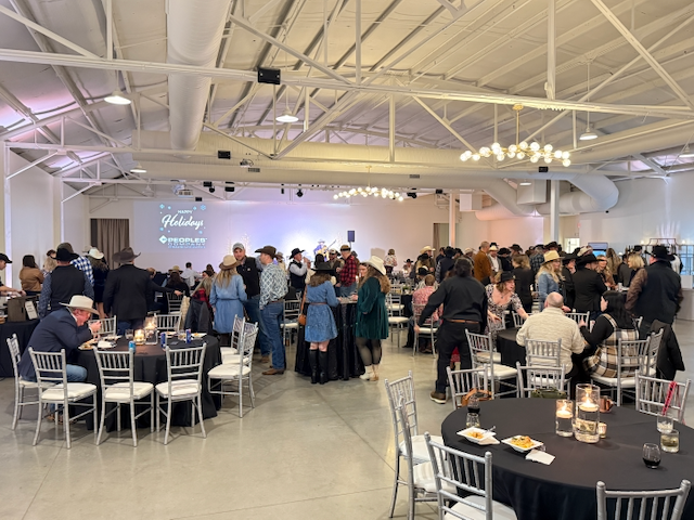 Large event space with people mingling at tables, many wearing cowboy hats.