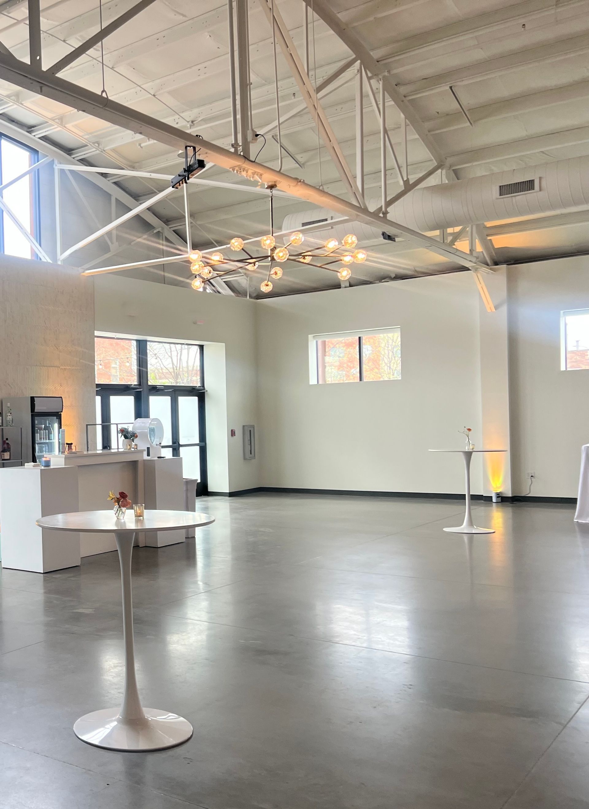 Spacious, empty white event room with a polished concrete floor, modern lighting, and a white bar.