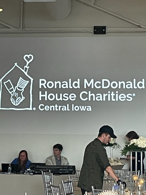 Ronald McDonald House Charities logo projected, event setting with people adjusting decorations.