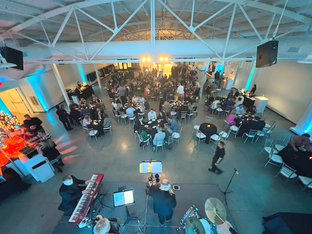 Event with band, tables, and people in a large venue with blue and white lighting.