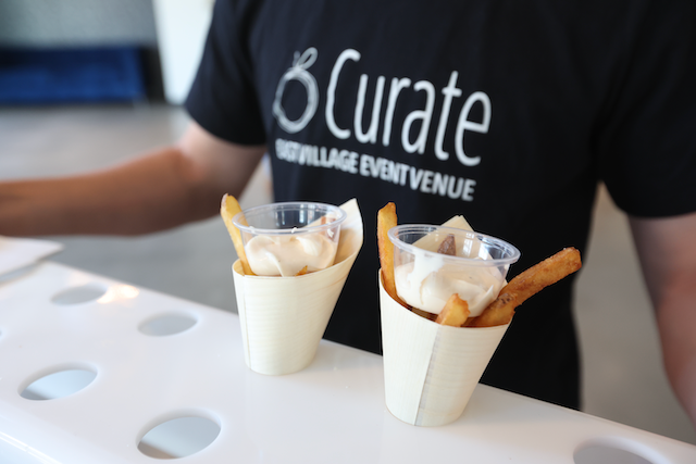 Two cups of fries with dip in white paper cones on a white surface, with a person wearing a 