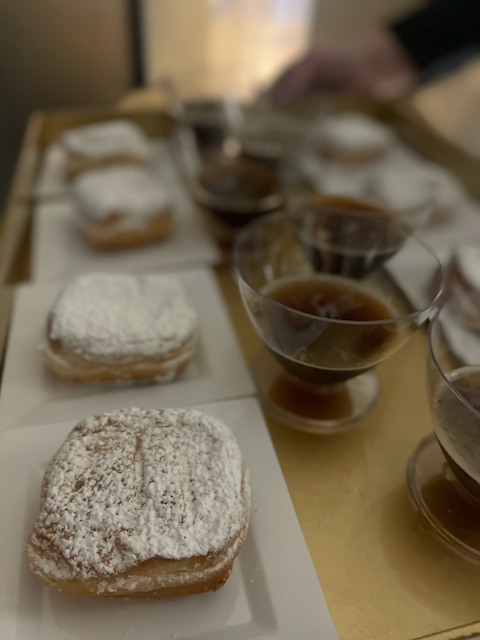 Beignets dusted with powdered sugar and coffee in small glass cups on a tray.