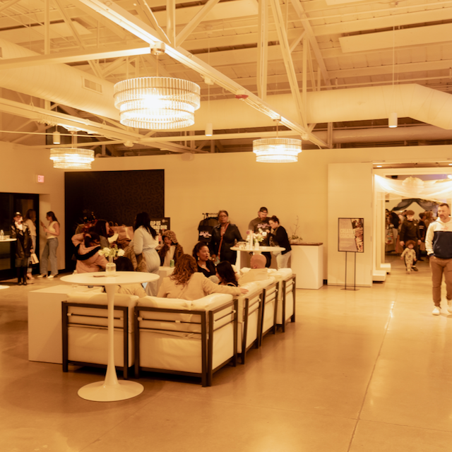 Event space with people socializing, couches, tables, chandeliers, and white walls.