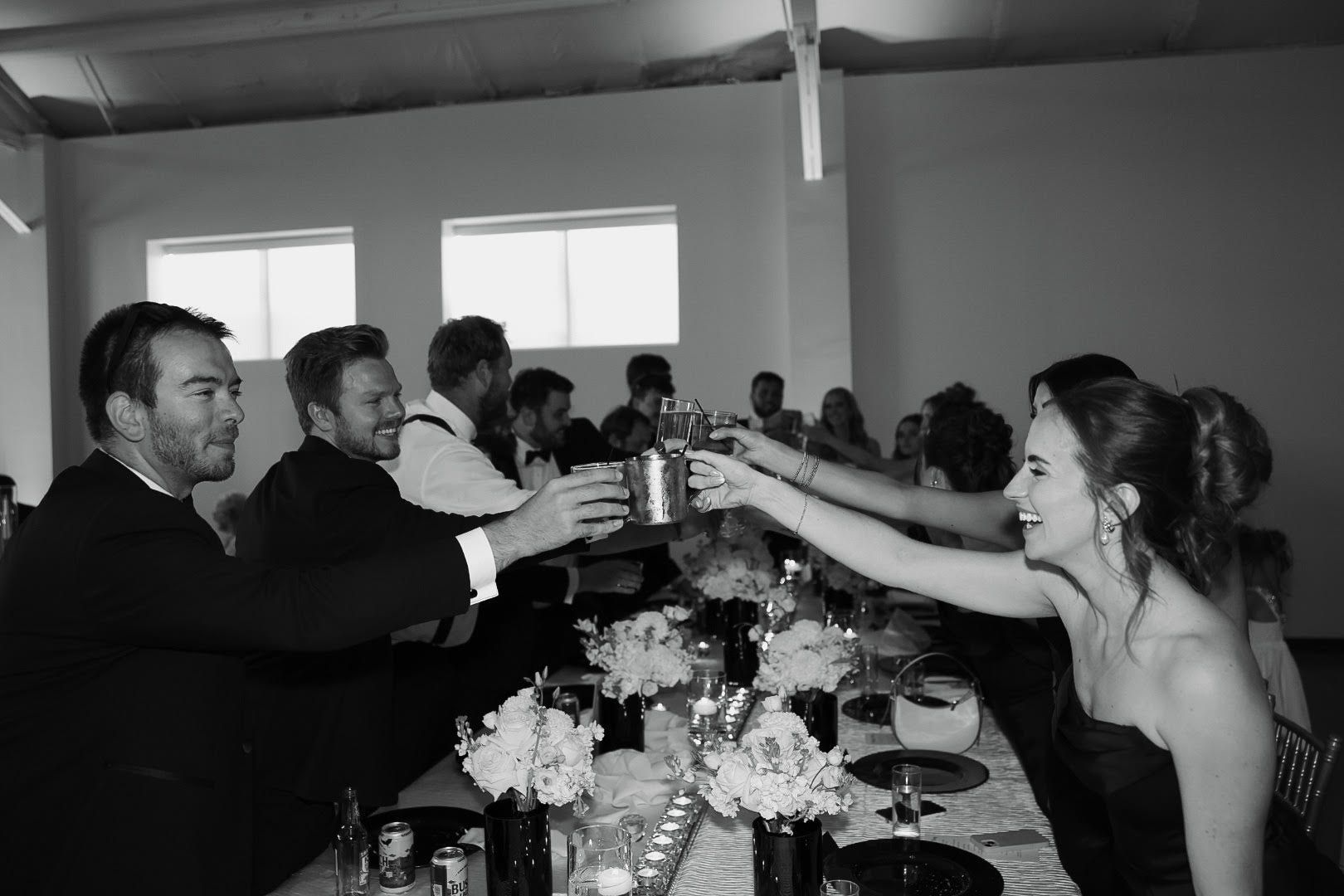 Guests in formal wear toast across a long banquet table at a lively indoor celebration.
