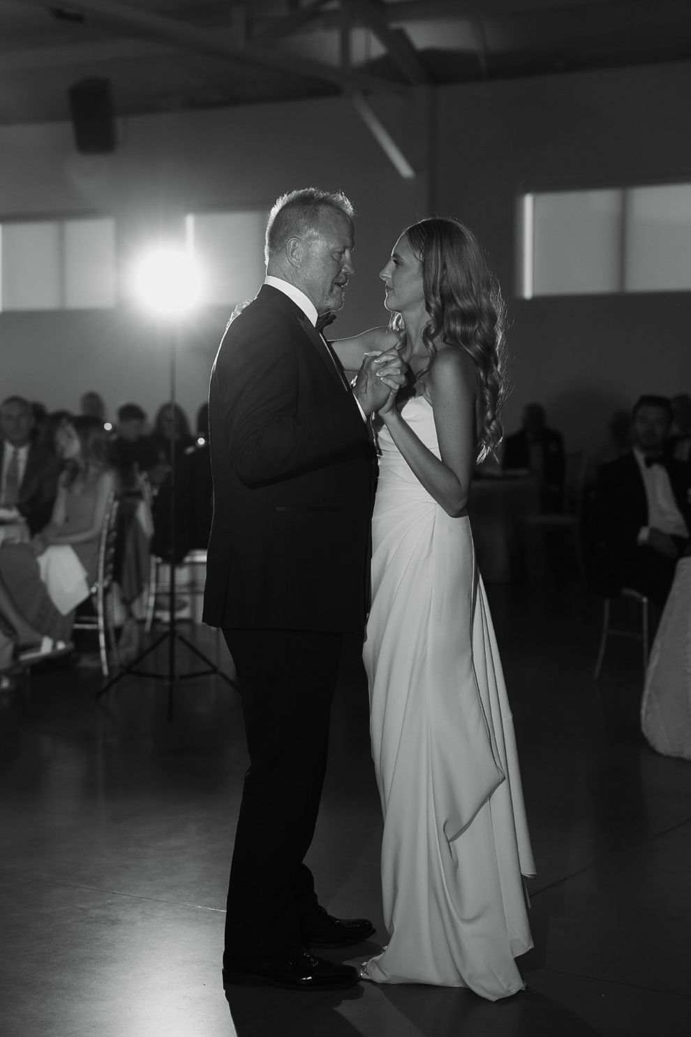 Couple dancing at a formal event, with the woman in a light dress and the man in a dark suit.