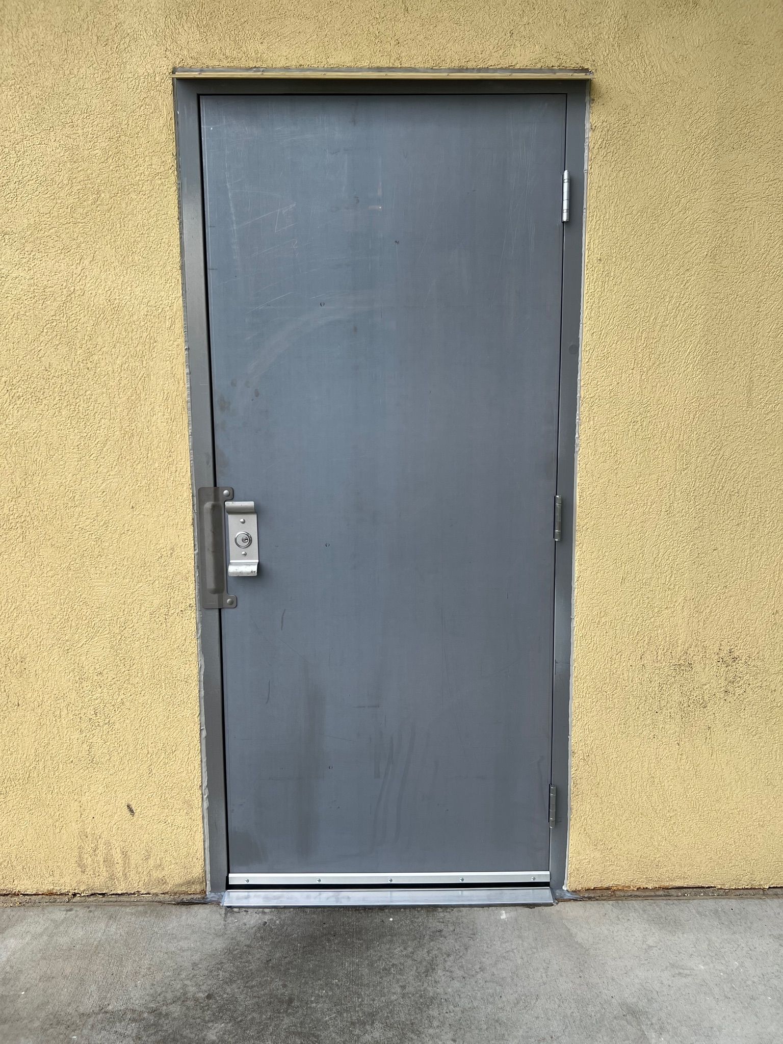 Gray metal door with keypad on a yellow stucco wall.