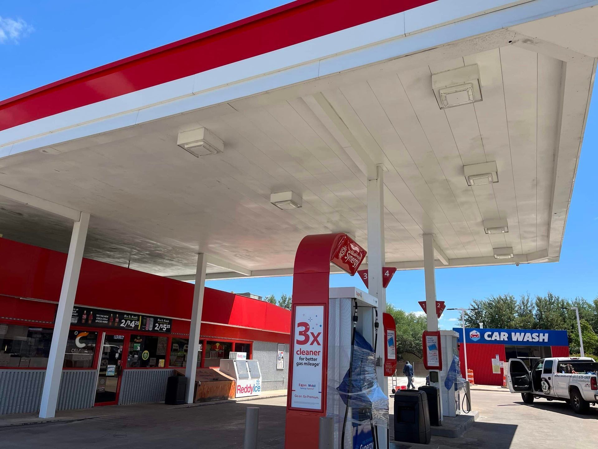 Gas station canopy with red trim, pumps, and a car wash under a bright blue sky.