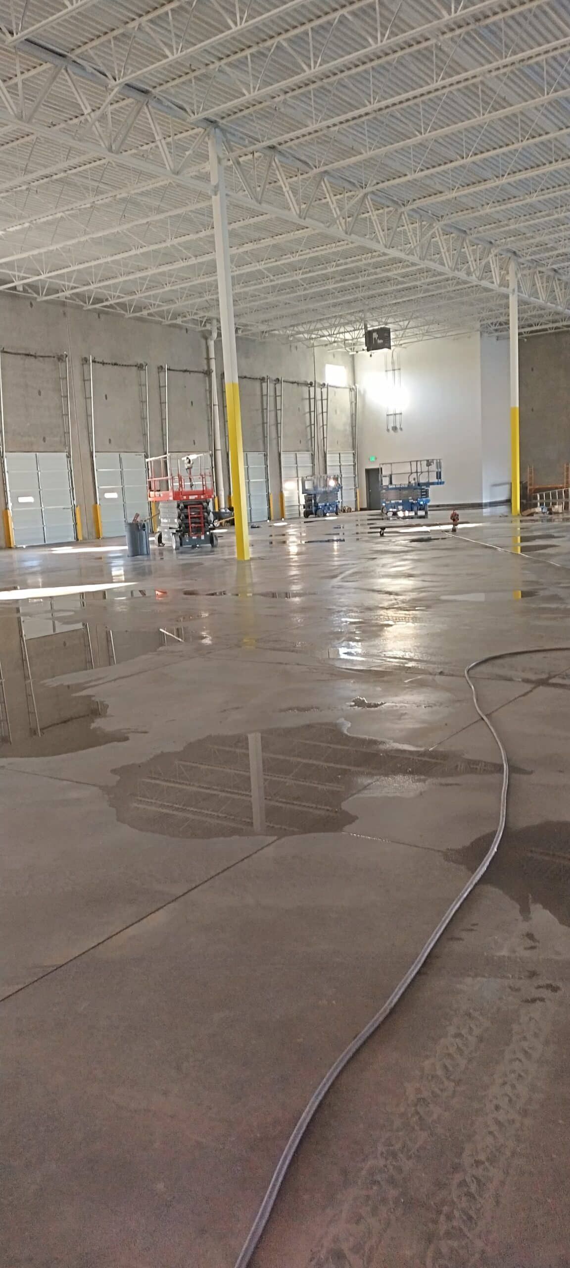 Interior of a large industrial building; wet concrete floor reflects overhead lights.