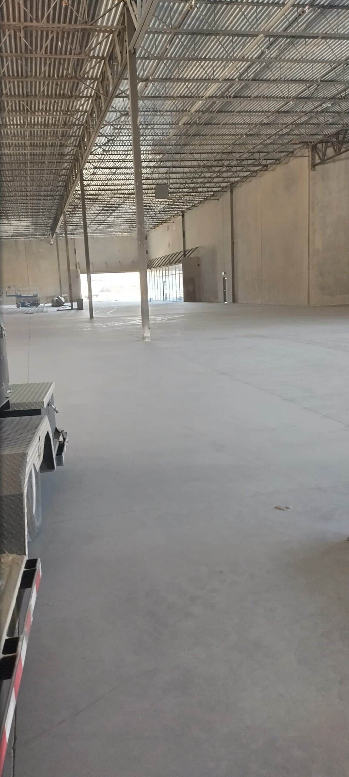 Inside a large, empty warehouse, showing the ceiling beams and concrete floor.