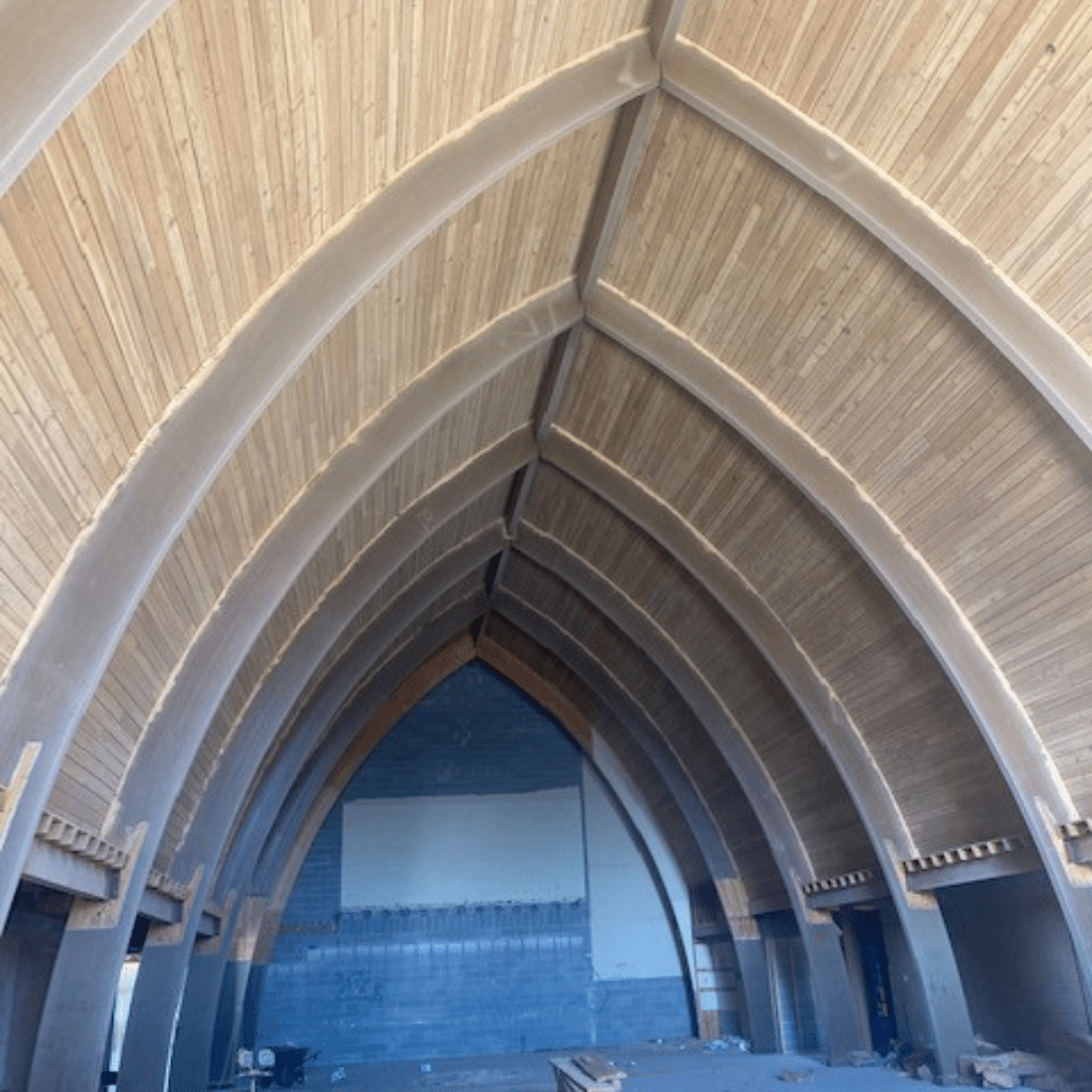 Interior view of a building with arched ceiling and gray concrete ribs, and light wooden paneling.