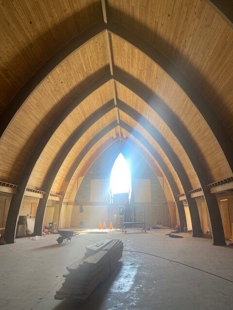 Interior view of a building under construction. Arched wooden ceiling, bright light in the center, concrete floor.