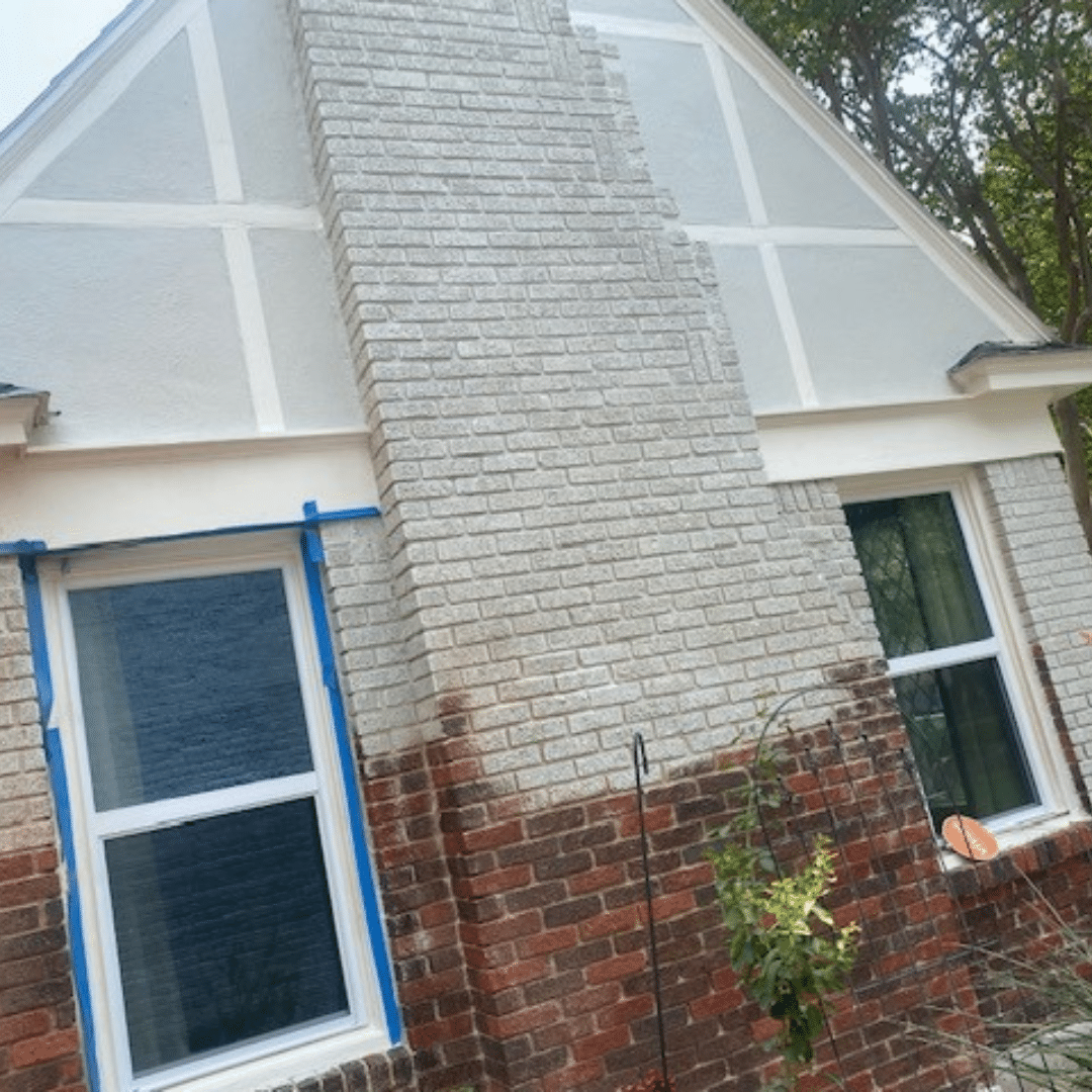 A house with a painted brick chimney and windows, some with blue painter's tape.