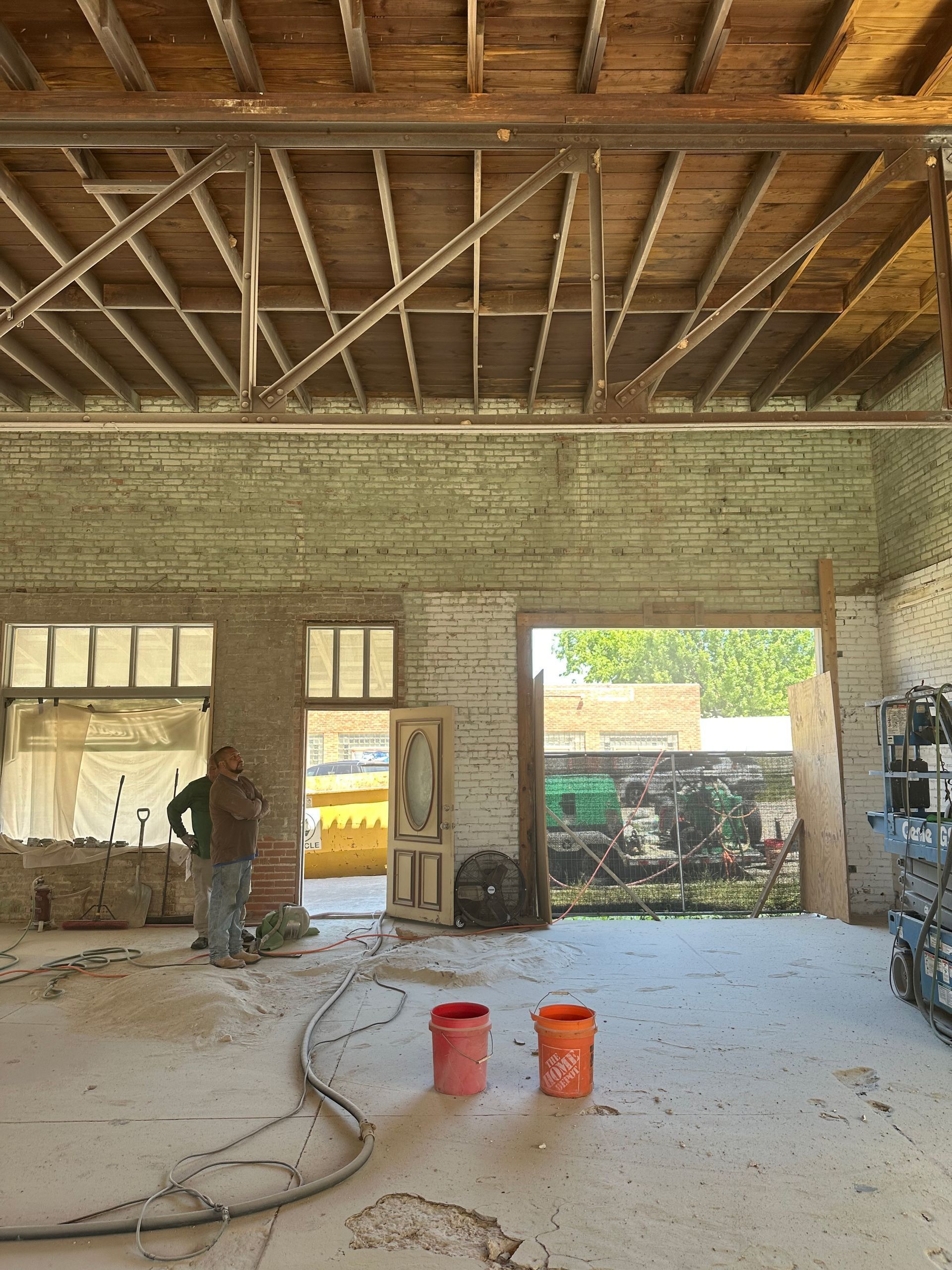 Interior of a building under renovation; man stands near red buckets; open doorway.