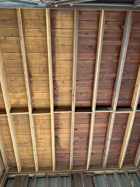 Wooden ceiling with exposed beams, showing a contrast between lighter and darker wood tones.