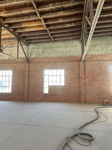 Empty brick-walled industrial interior. Concrete floor, wooden ceiling with metal beams, windows.