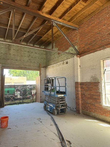 Interior of a brick building under renovation, with a lift, open doorway, and exposed beams.