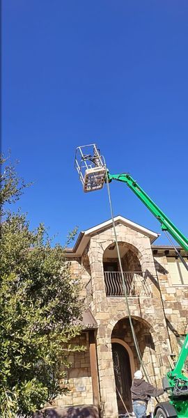 Green lift platform near a stone building, person in the basket. Clear blue sky.