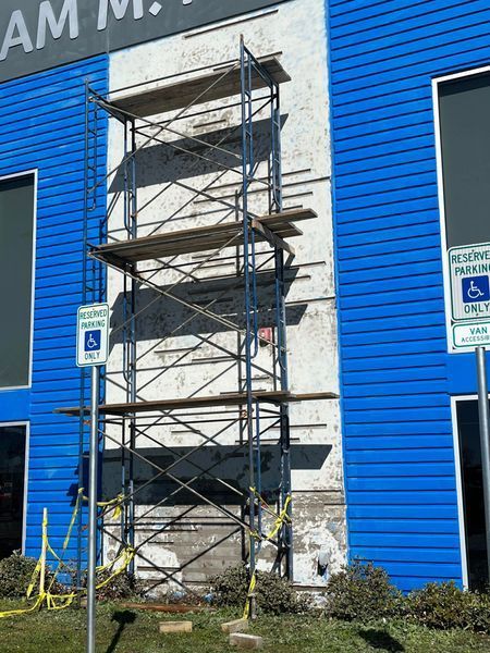 Scaffolding on white wall of a blue building with reserved parking signs.
