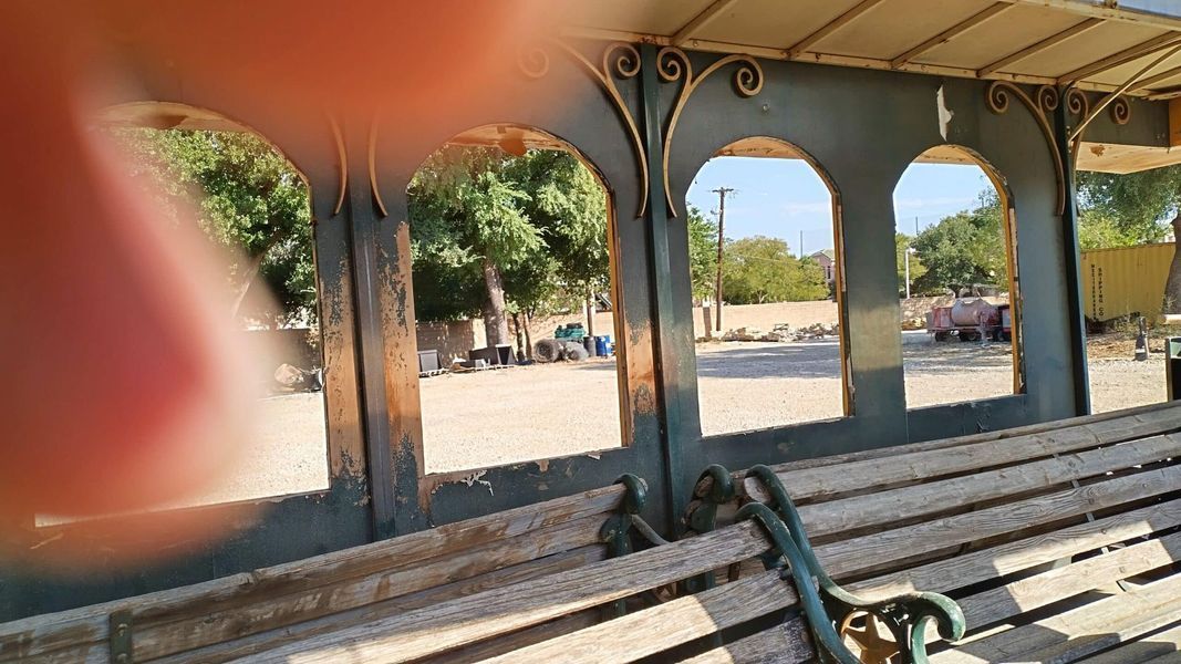 View through archway of wooden bench with metal frame; exterior scene of park with trees and people.