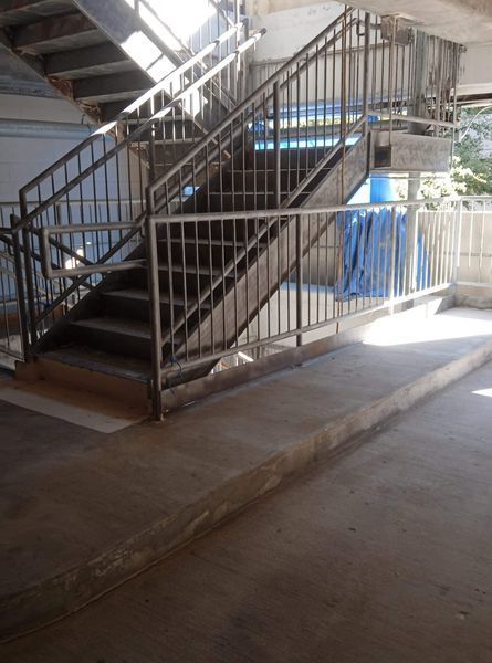 Staircase with metal railings and a concrete ramp; indoor, gray and white.