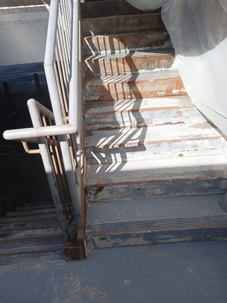 Staircase with peeling paint, metal railing, and strong shadow from above.