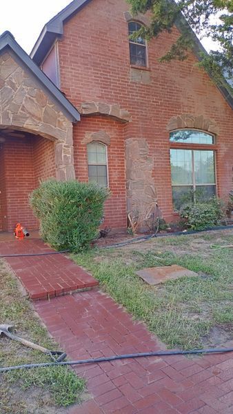 Brick house exterior with stone accents, red brick walkway, green bushes.