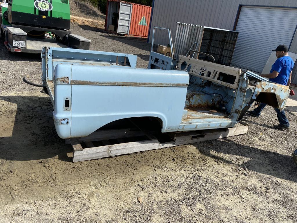 A light blue truck bed shell on wood pallets with a person carrying a metal piece.