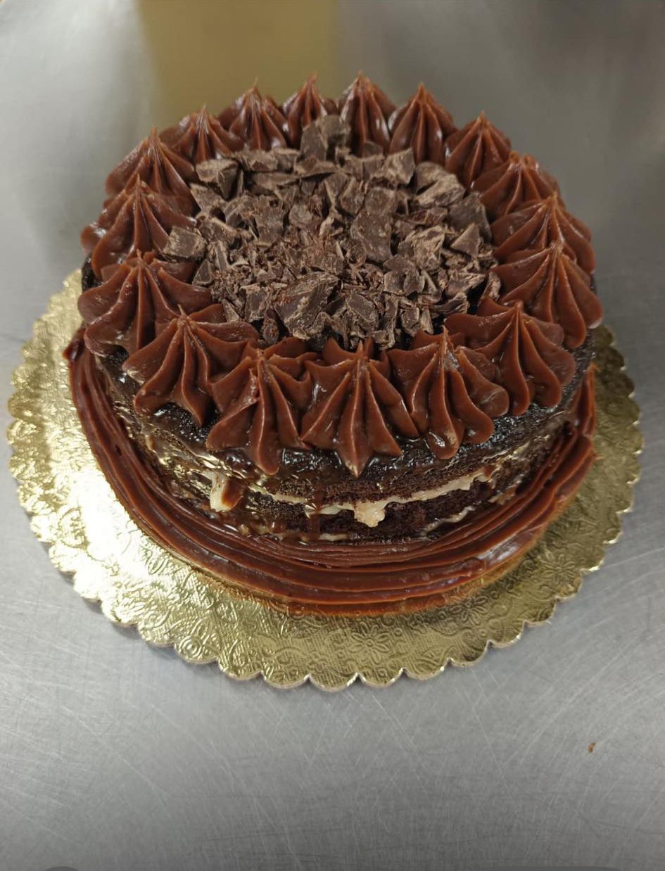 A chocolate layer cake with piped frosting rosettes and chocolate shavings on a gold scalloped cake board.