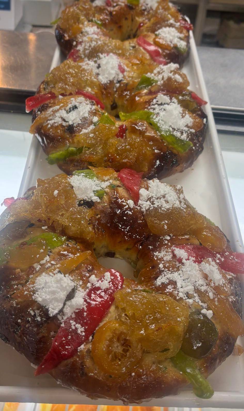 Three ring-shaped fruit cakes garnished with candied fruit and powdered sugar arranged on a white tray.