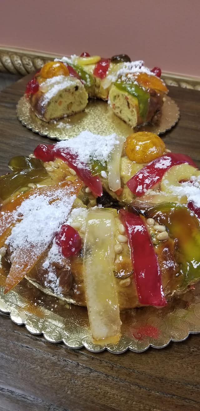 Two colorful, ring-shaped cakes with candied fruit, dusted with powdered sugar, on gold-edged plates.