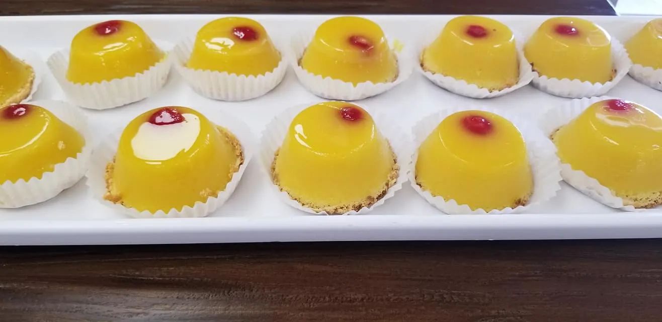 Yellow glazed pastries in paper cups on a white platter. A dark wood table is in the background.