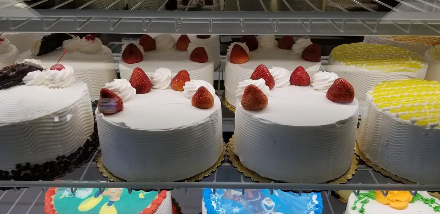 Cakes in a display case. Some are decorated with strawberries. Others have white frosting and no toppings.