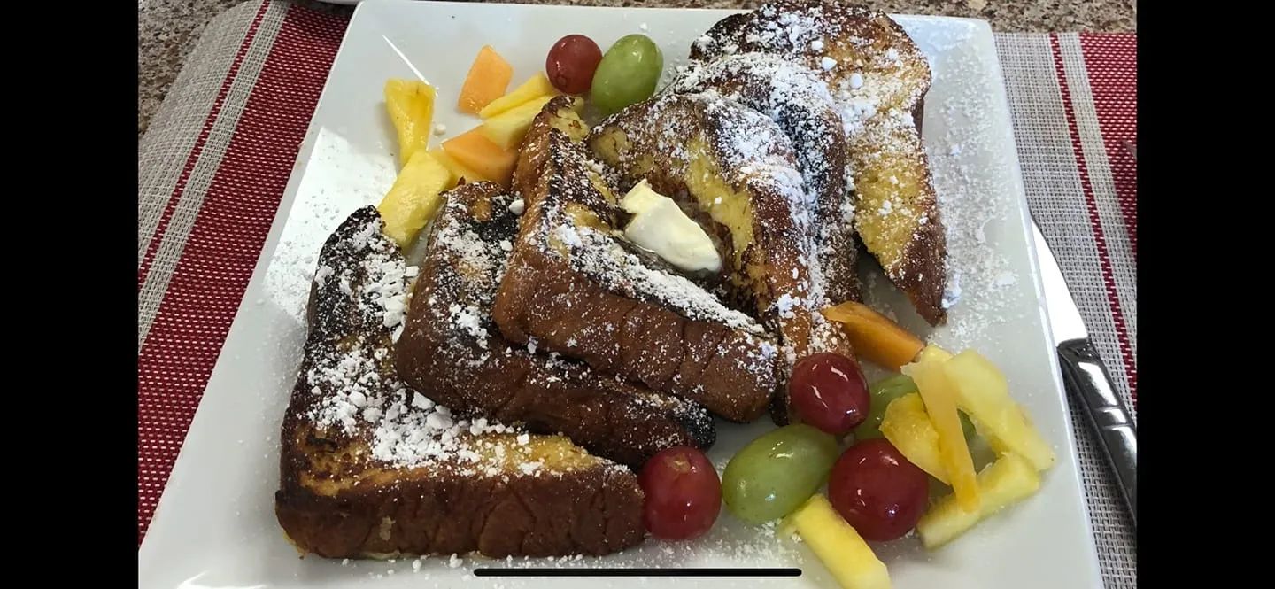 French toast with fruit on a white plate, dusted with powdered sugar.
