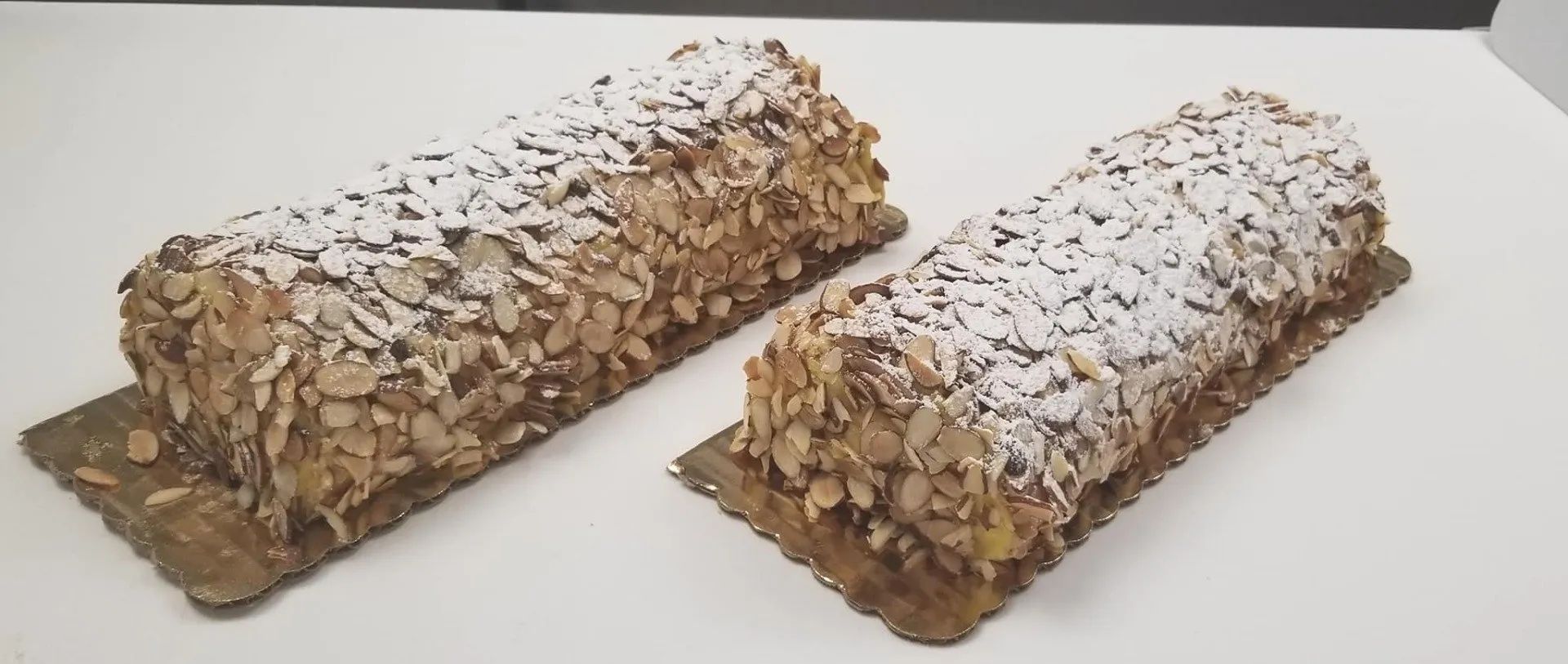 Two almond-covered pastries dusted with powdered sugar on a white surface.