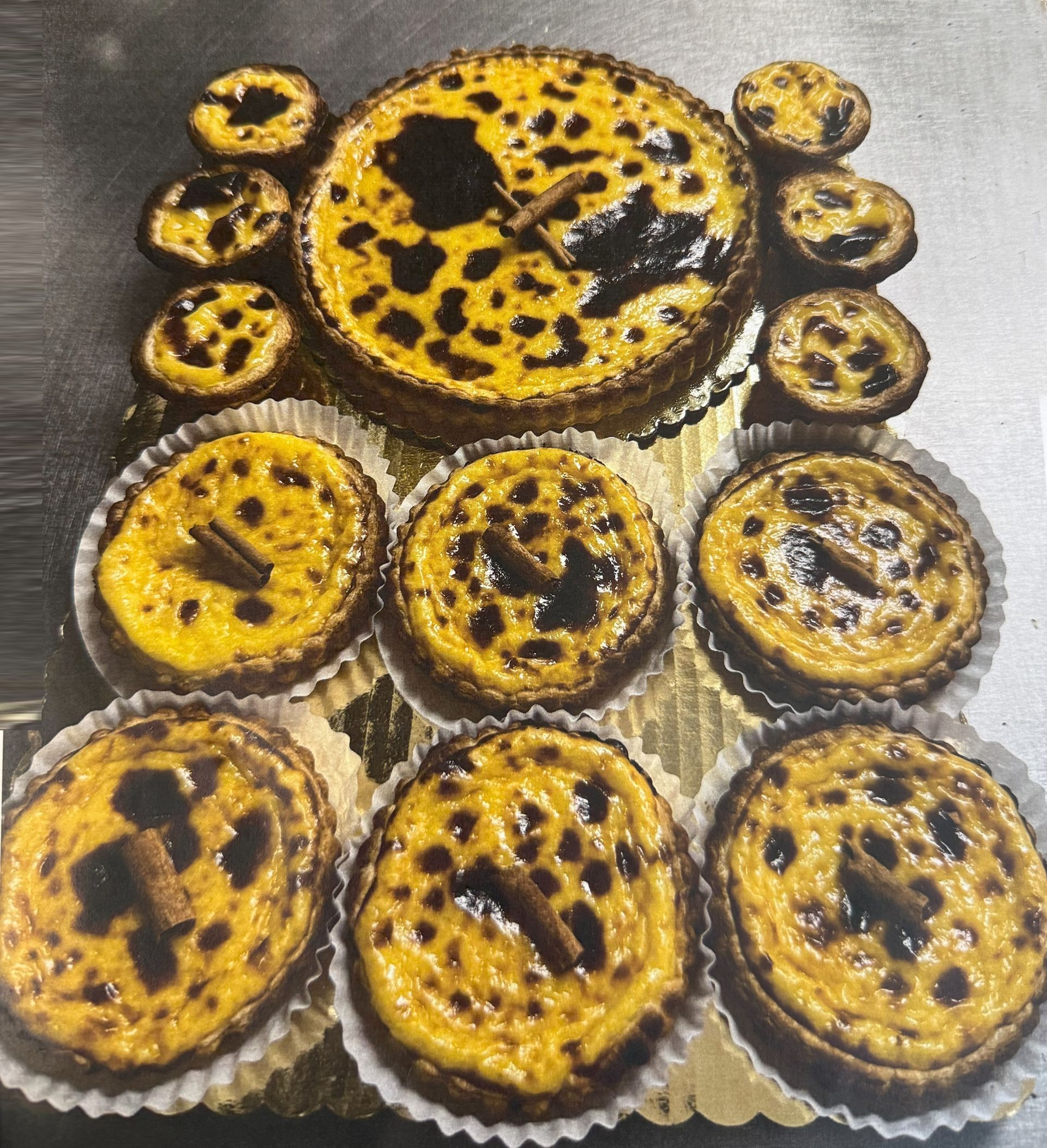Pastéis de Nata, Portuguese custard tarts, arranged on a golden platter; golden crusts, dark custard centers, cinnamon sticks.