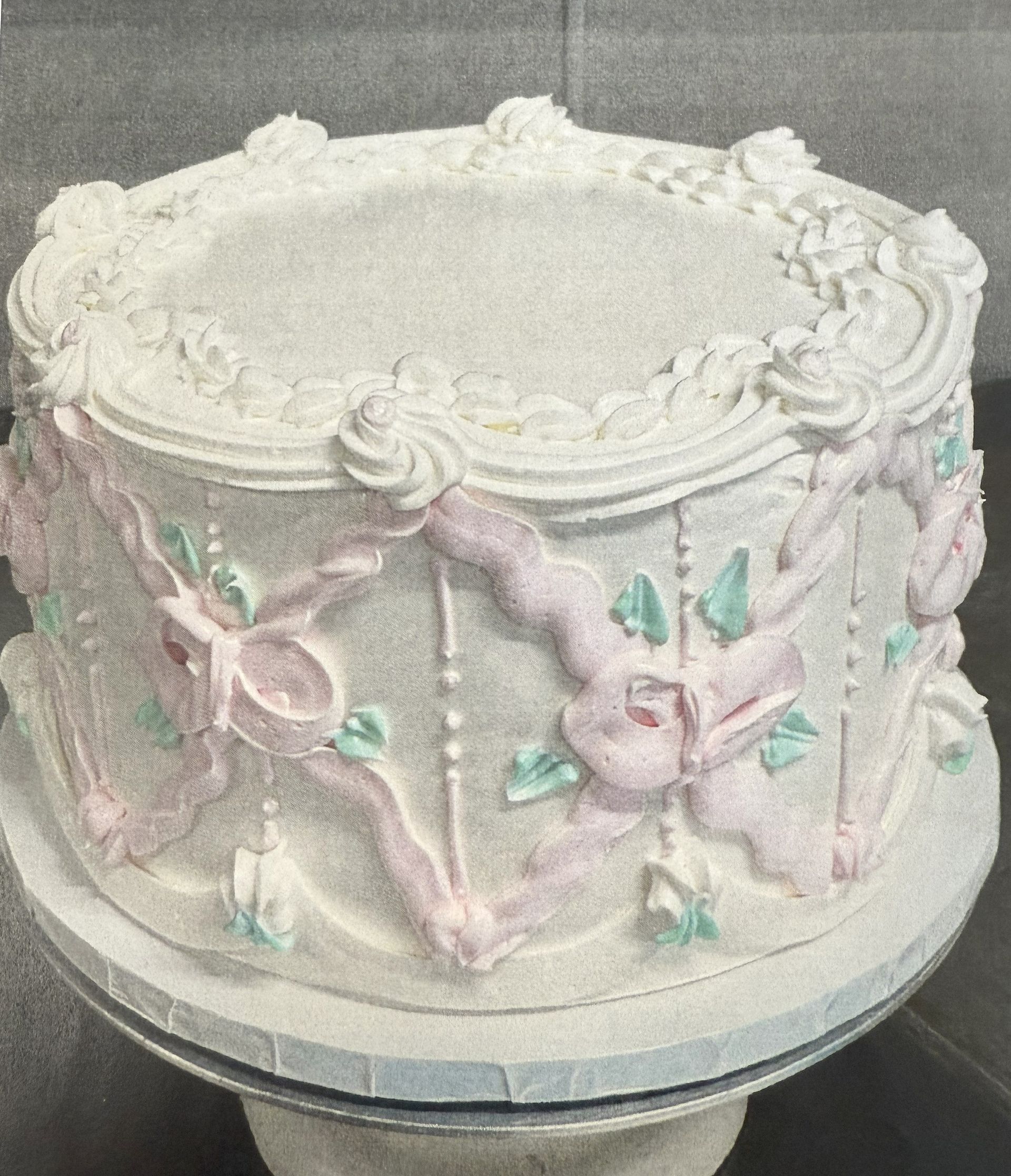 White cake with pink ribbons, green leaves, and piped frosting details.