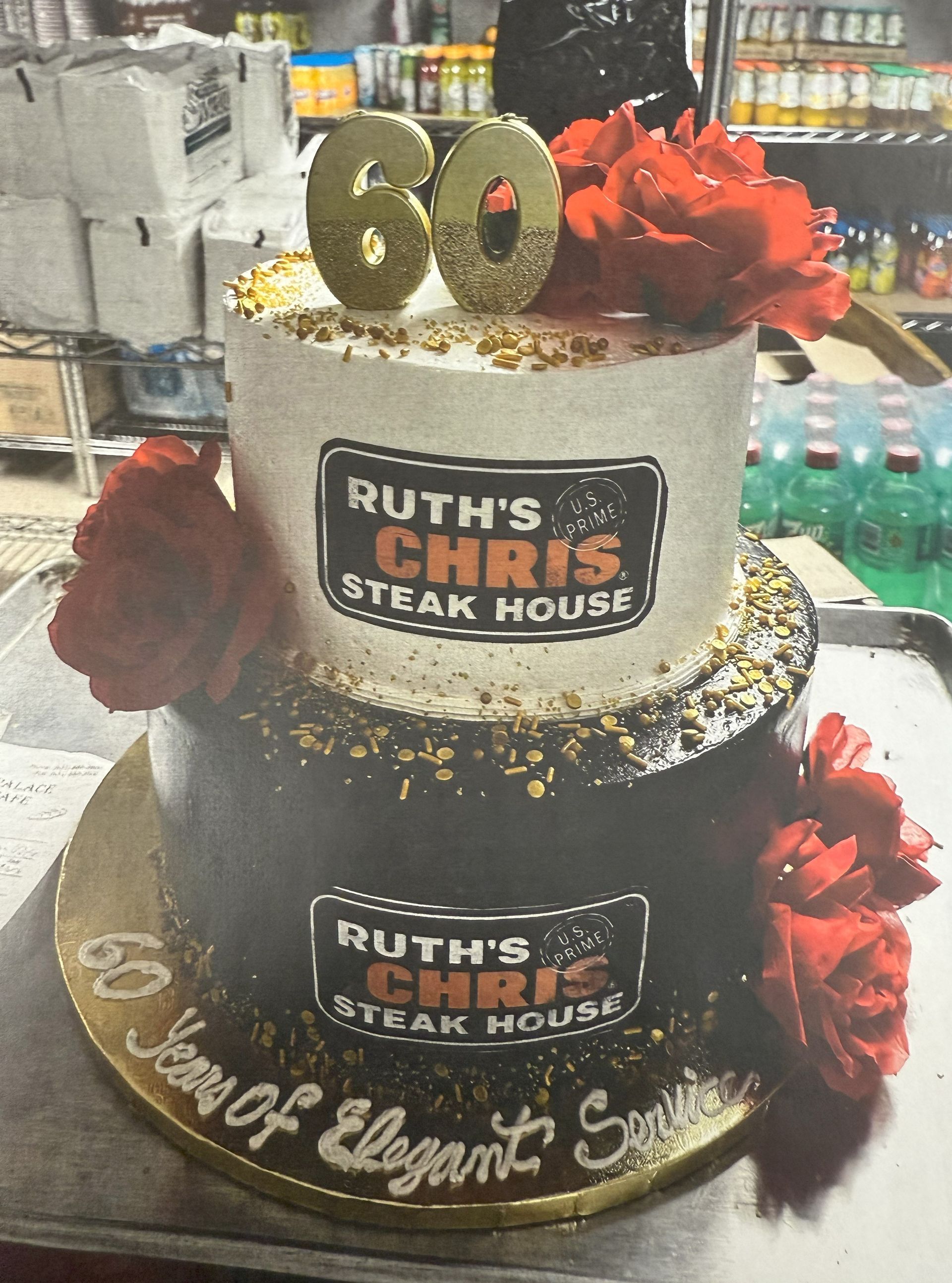 Two-tiered cake for Ruth's Chris Steak House 60th anniversary, decorated with red flowers and logo.