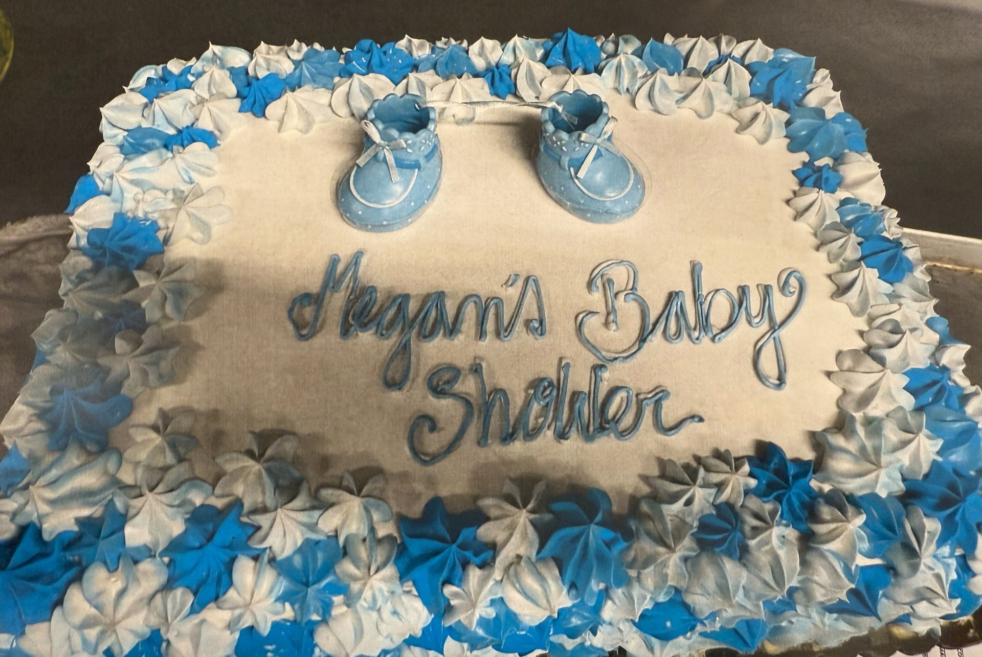 Baby shower cake with blue and white frosting, baby shoes, and text that reads 
