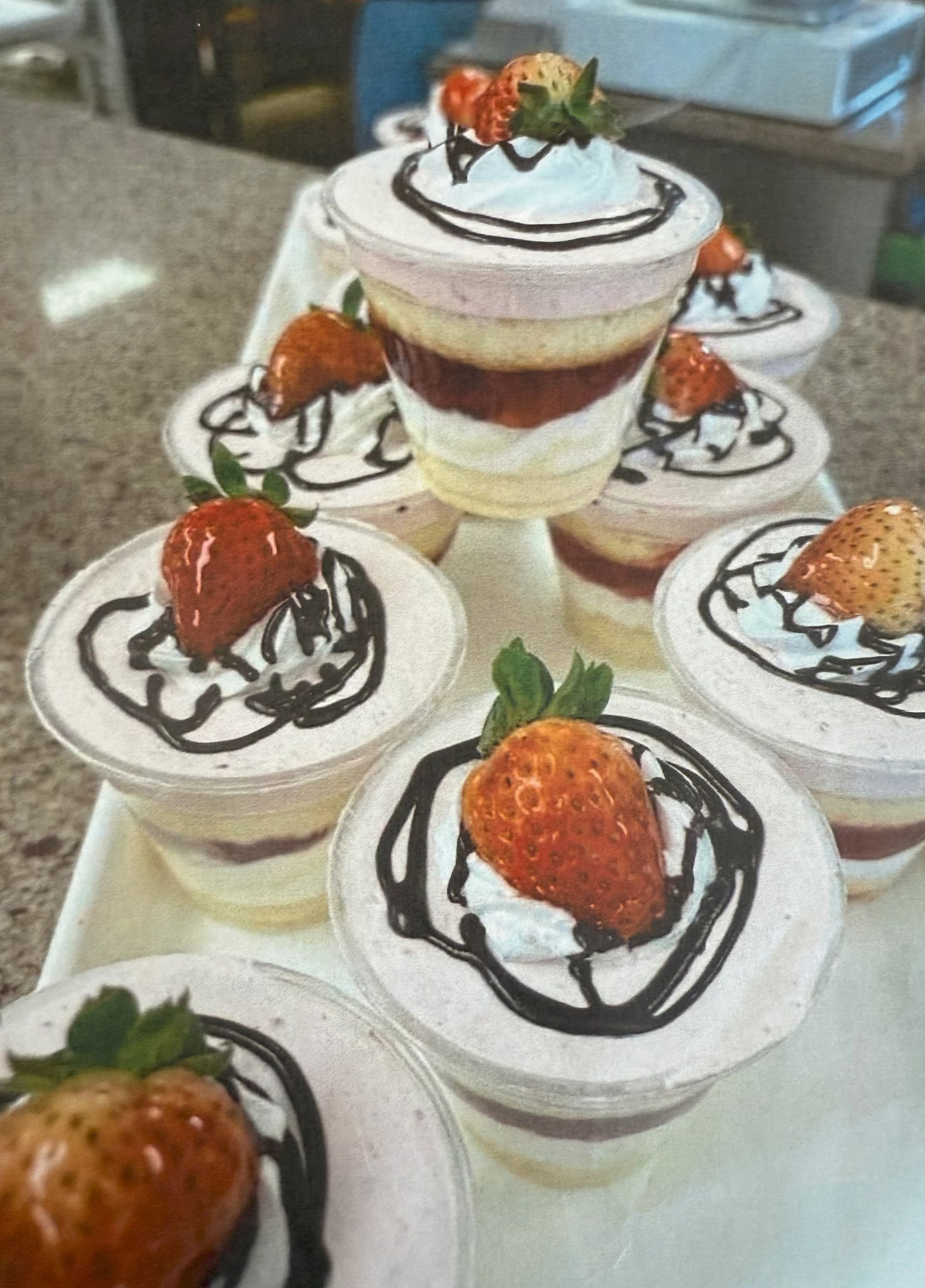 Strawberry parfait desserts in clear cups, drizzled with chocolate and topped with whipped cream and fresh strawberries.