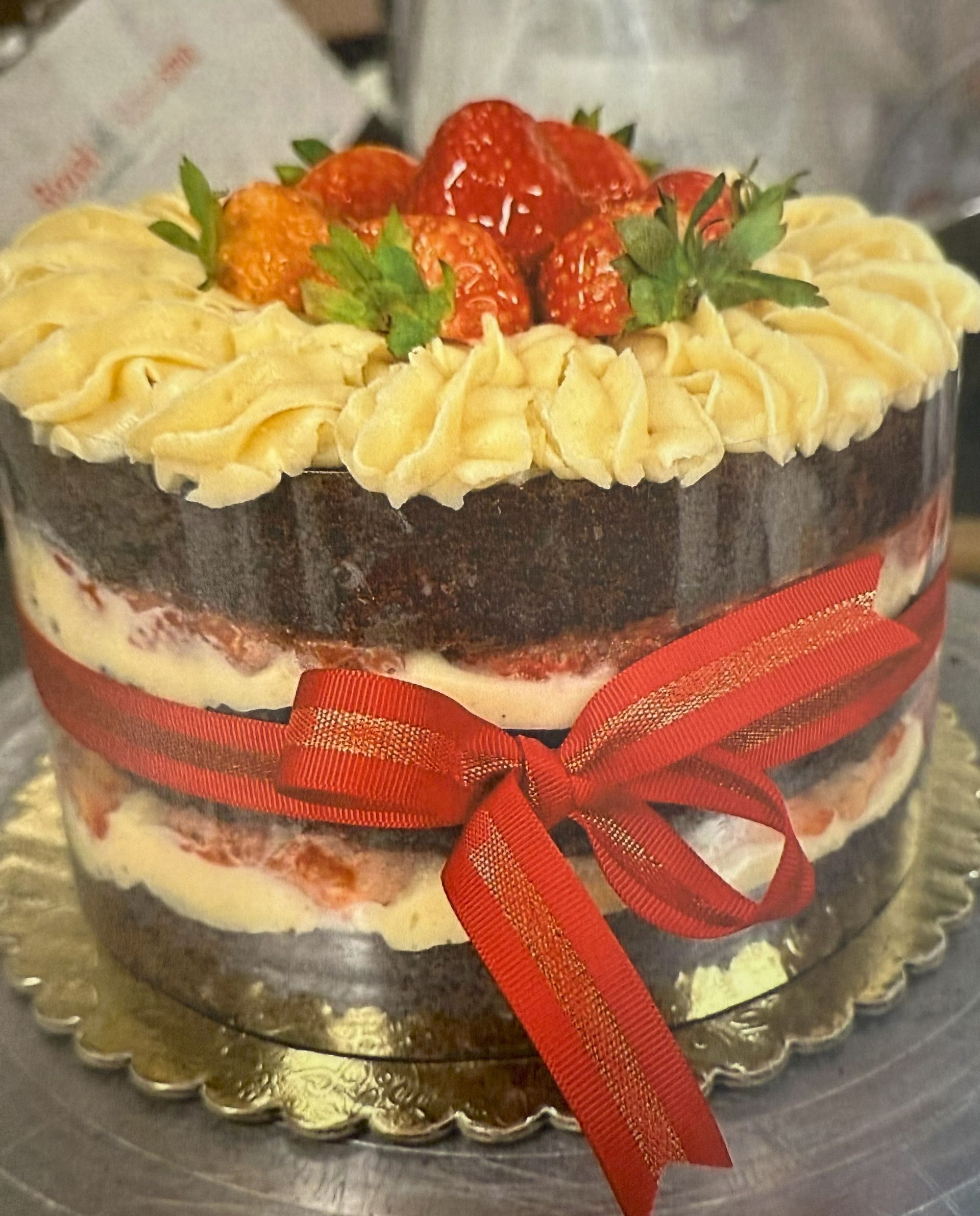 Chocolate cake with frosting, strawberries, and red ribbon.