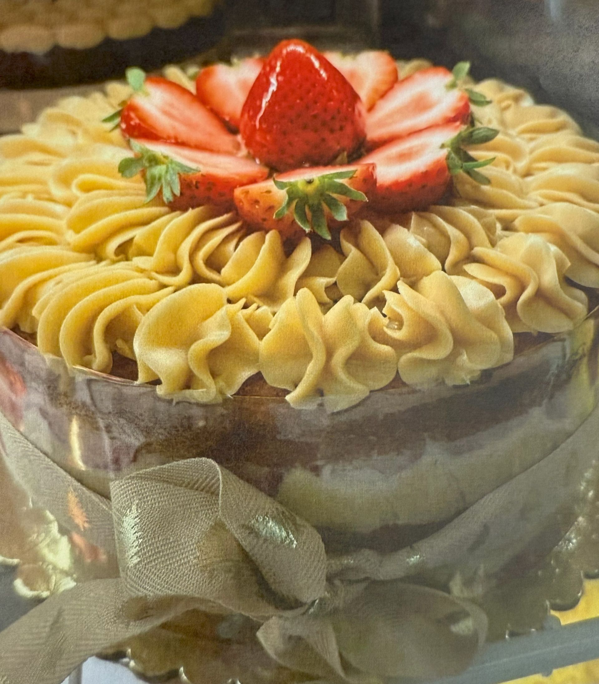 Cake with strawberry topping and piped frosting, wrapped with a gold ribbon.
